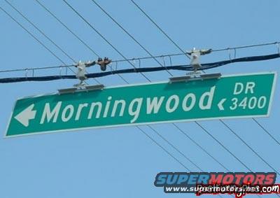 Green street sign reading "Morningwood DR 3400" with a left arrow, against a blue sky and power lines