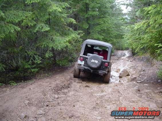 Jeep Wrangler driving on a muddy, rocky trail through a forest