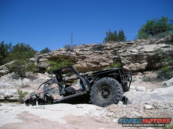 Off-road vehicle with camouflage paint and roll cage navigating rocky terrain