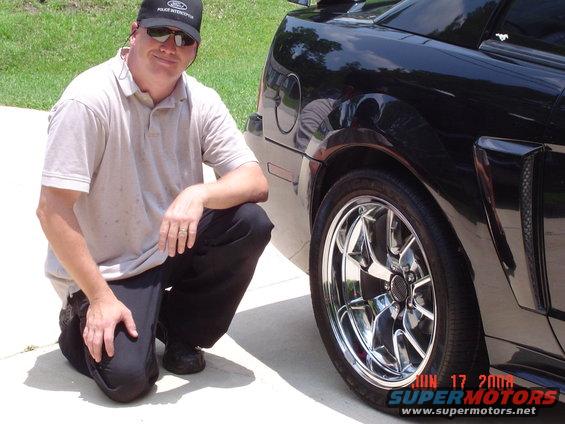 Black car's rear wheel and side panel, with a man kneeling beside it