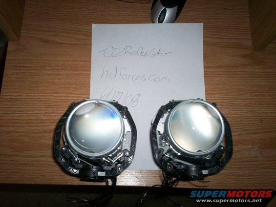 Two projector headlights on a wooden surface with a paper note