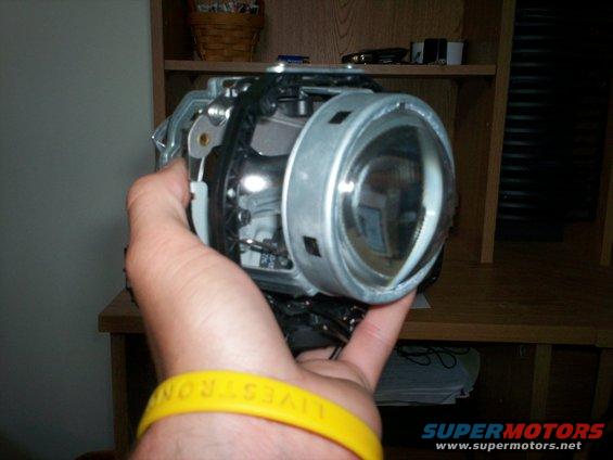 Hand holding a car headlight projector assembly, showing the lens and internal components