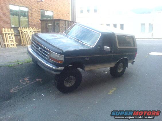 Dark blue Ford Bronco with a tan top, lifted on large tires, parked on asphalt