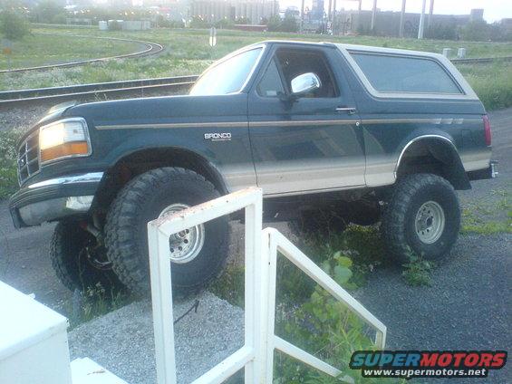 Green Ford Bronco with tan lower body panels and large tires parked on gravel