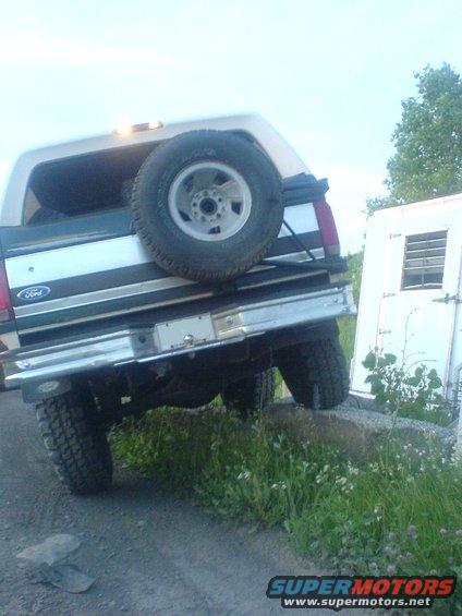Ford Bronco parked on a rock with a spare tire mounted on the back. A white trailer is to the right