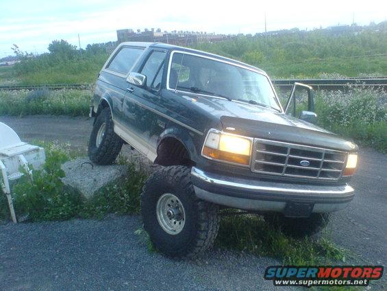 Dark green Ford Bronco with lifted suspension and large tires, parked on gravel and grass