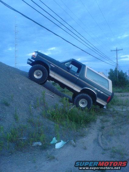 Dark blue and tan 1985 Ford Bronco climbing a dirt hill