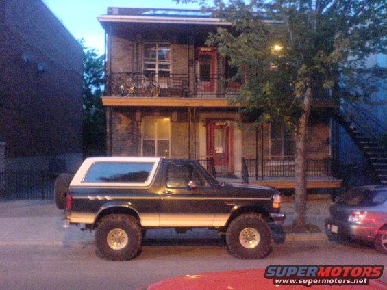 Black and white Ford Bronco with lifted suspension parked on street, another car visible to the right