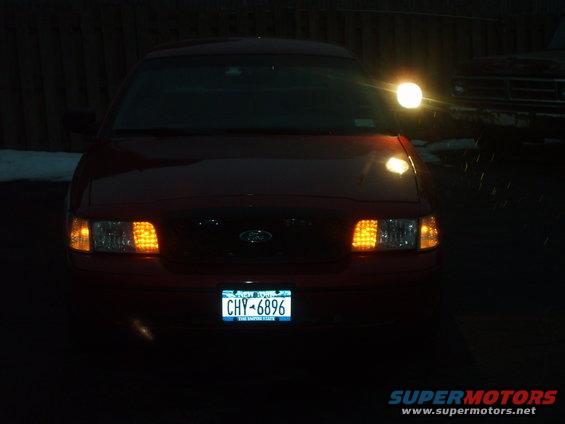 Red 2000 Ford Crown Victoria front view with headlights on