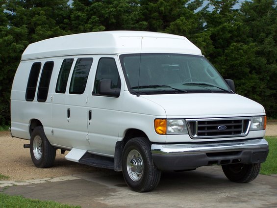 White Ford E250 van with a raised roof, parked outside with trees in the background