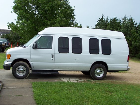 White van with tinted windows, parked on a concrete driveway next to grass. Side view