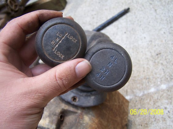 Hand holding two transfer case shifter knobs, one labeled LO, N, HI, LOCK and the other 4L, N, 2H, 4H