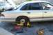 1992 Ford Crown Victoria - A car is up on a jack with its wheel removed, surrounded by tools, indicating maintenance is underway.