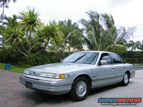 Silver 1992 Ford Crown Victoria sedan, front 3/4 view, parked on paved driveway with palm trees in background