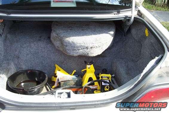Car trunk interior showing spare tire, oil drain pan, and yellow jack stands