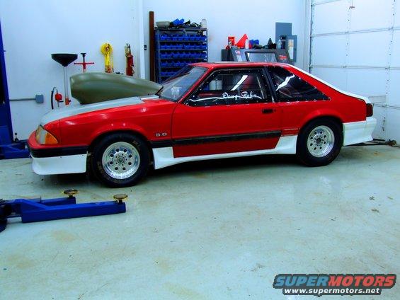 Red and white 1990 Ford Mustang with a grey hood, side view, in a garage