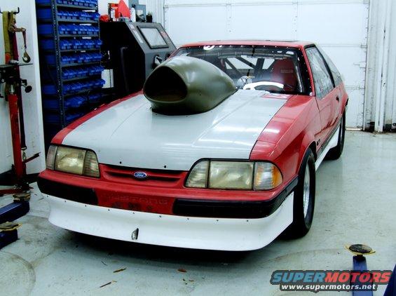 1990 Ford Mustang drag car with large hood scoop and roll cage, in a garage