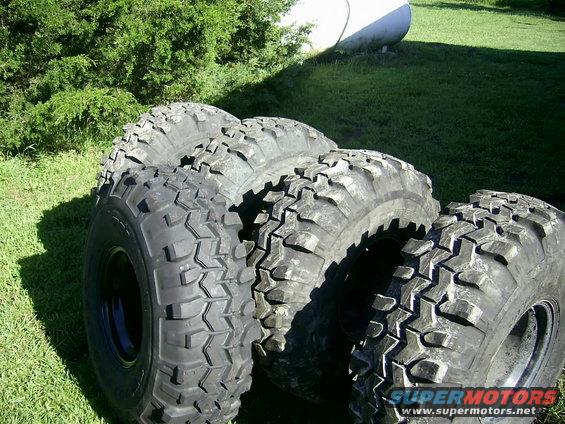 Four off-road tires with aggressive tread patterns are arranged on grass