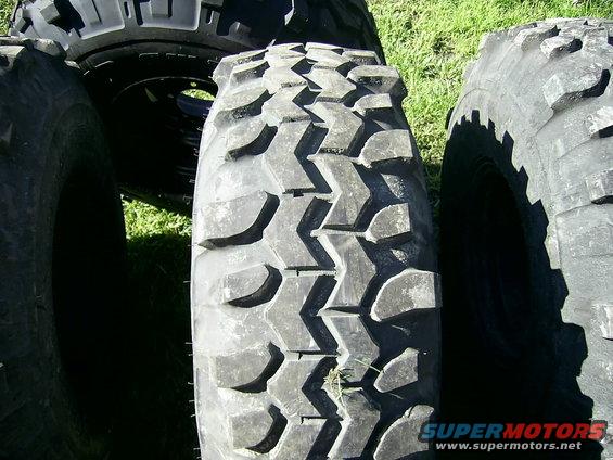 Close-up of aggressive off-road tires with deep treads, some grass visible