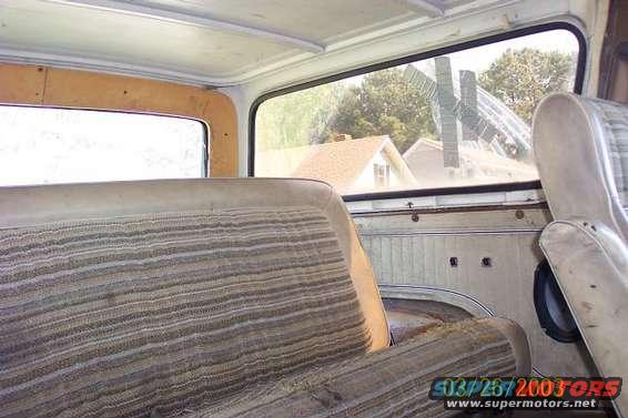 Interior shot of a vehicle, showing striped seats and door paneling. Houses visible through the window