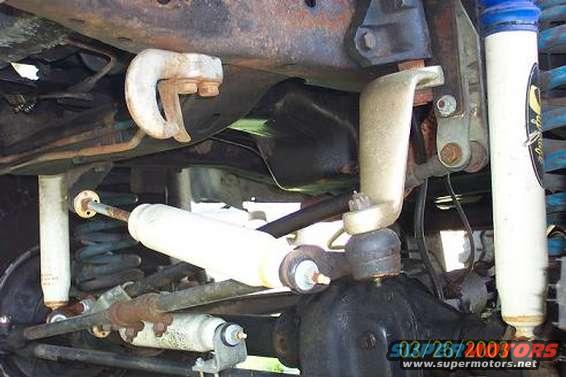 Undercarriage of a vehicle with visible suspension components, shocks, and differential. Rusty metal parts are prominent