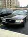 1999 Ford Taurus - A black Ford Crown Victoria is parked in a lot, with a building in the background.