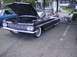 1970 Ford Ranchero - A classic black 1959 Chevrolet Impala is displayed with its hood open, while a man relaxes in a chair beside it.