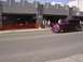 1970 Ford Ranchero - A maroon sedan drives down the street in front of a building with outdoor seating.