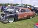 1970 Ford Ranchero - Customized sedan with a rusty patina and lowered stance sits on display at a car show.
