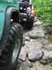 1967 Ford Bronco - Two off-road vehicles tackle a challenging rocky and muddy trail through a wooded area.