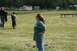 1990 Chevrolet Suburban - A woman stands in a field, with people and buildings in the background.