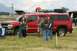 1990 Chevrolet Suburban - A group of people gather around a red pickup truck with a camper shell, with mountains visible in the distance.