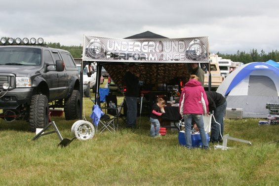Lifted dark gray SUV with roof lights parked next to a tent with 'Underground Performance' banner