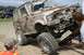 1990 Chevrolet Suburban - An off-road SUV, heavily covered in mud, navigates a ramp during an event, with another vehicle visible in the background.