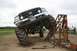 1990 Chevrolet Suburban - A modified black Ford truck with oversized tires is positioned on a metal ramp during an event.