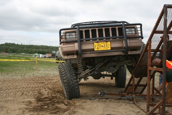 Modified Jeep Cherokee XJ with large tires and bull bar, front view, on sandy terrain