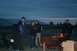 1990 Chevrolet Suburban - A group of people gather around a fire pit as the sky darkens, with a large structure visible in the distance.