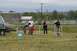 1990 Chevrolet Suburban - A group of people gather in a grassy field near a fence and buildings.