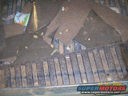 Truck bed with torn carpet and debris, including a small bag. The bed liner is visible