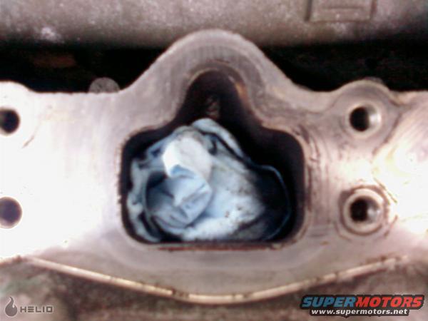 Engine intake manifold port stuffed with a blue rag. Metal casting shows bolt holes