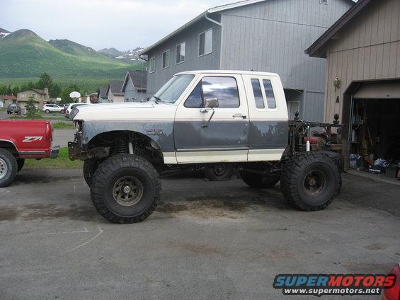 1990 Ford F-250 pickup truck with lifted suspension and large tires, parked next to a red pickup truck
