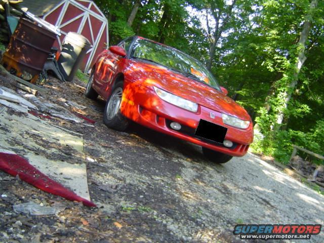 Red 1997 Saturn SC coupe parked on a gravel driveway with a red barn in the background