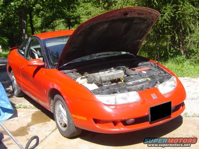 red coupe, hood up, showing engine bay. License plate is blacked out. Supermotors.net logo visible