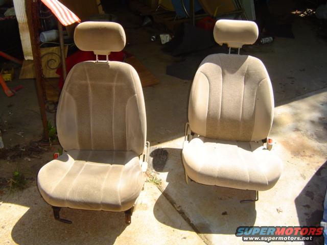 Two tan car seats with headrests sit on a concrete surface