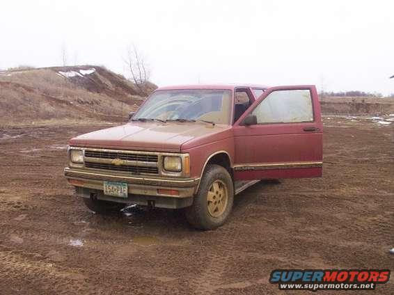 Red pickup truck, possibly a Chevrolet S-10, parked in a muddy field with driver's door open. License plate reads 154-PIE