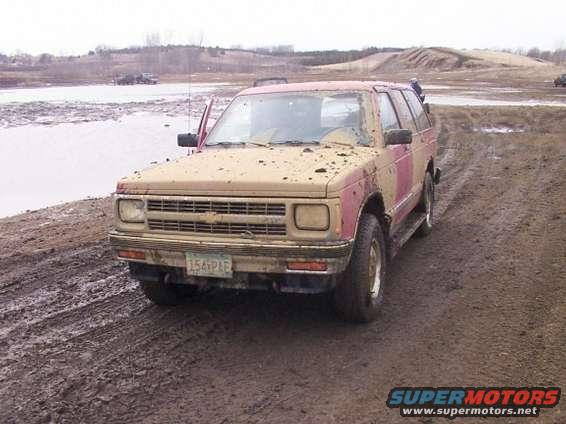 Muddy SUV with its door open, parked on a dirt track next to a body of water