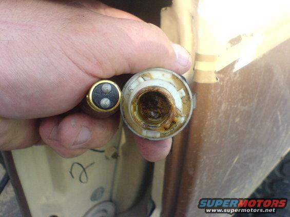 Hand holding a corroded light bulb socket and a two-pin bulb against a tan vehicle exterior