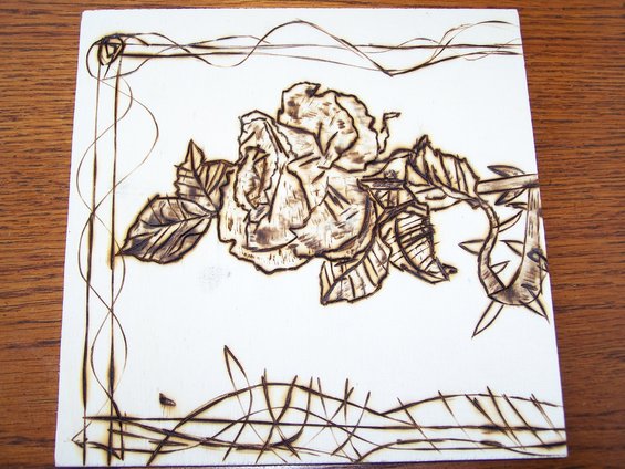 Pyrography art of a rose with leaves and thorns on a white surface