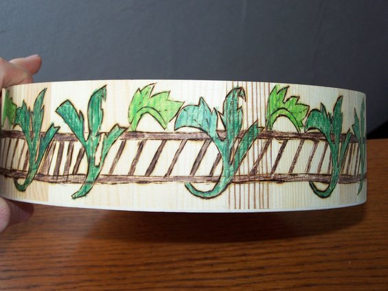 Wooden cylinder with pyrographic art of green leaves and a fence pattern