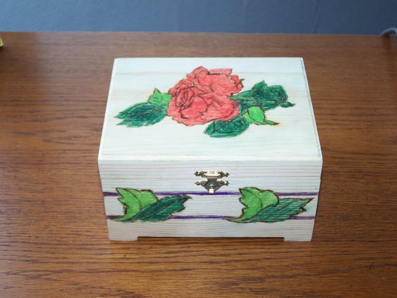 Wooden box with a red rose and green leaves painted on top. Purple stripes and green leaves on the side